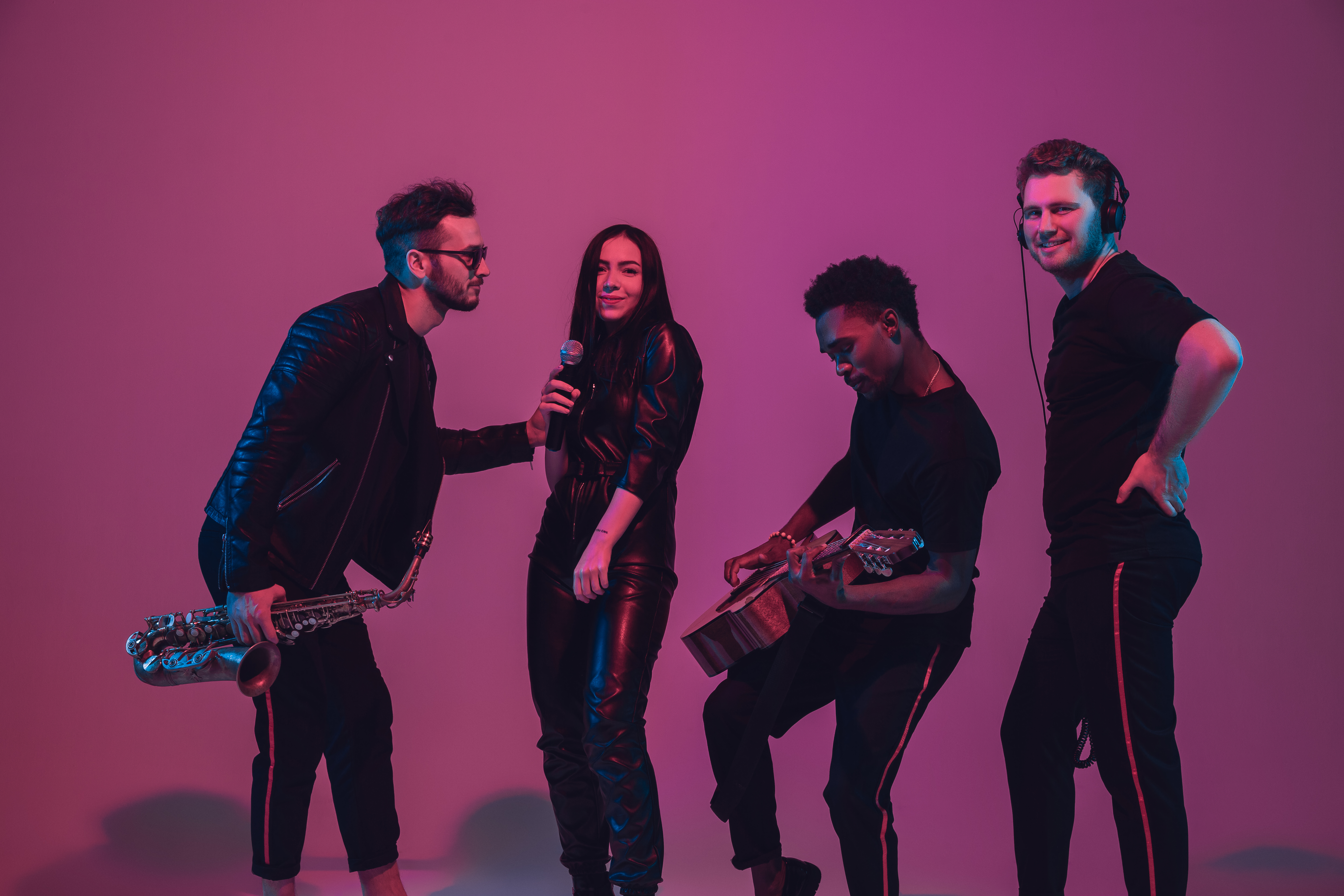 Group of young multiethnic musicians created band, dancing in neon light on pink background
